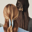 Four women shown from behind wearing tailored outerwear, standing against a plain light beige studio background. Their hair is in varied colors and lengths, including dark brown, curly auburn, light brown, and dark brown, with some styled with hair accessories.